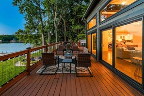 A deck with outdoor furniture, a view of a lake, and a building with large windows. - Normandy Approach w/Optional Boat Rental (Mooresville)
