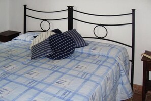 A bed with a metal frame, a blue checkered bedspread, and two striped pillows.