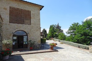 A stone building with a large arched entrance, outdoor seating, and potted plants.