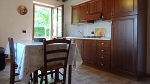A kitchen with wooden cabinets, a dining table with chairs, and a window with a view of greenery.