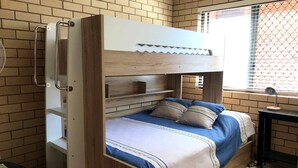 Un lit superposé avec une structure en bois, un ventilateur et une fenêtre avec des stores.