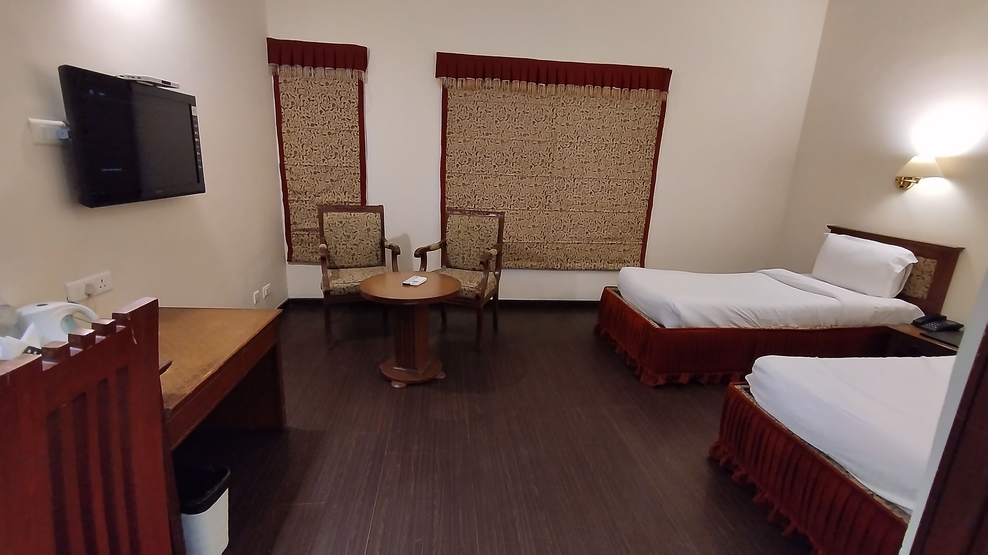 A hotel room with a bed, a desk with a chair, a television, and a window with curtains.