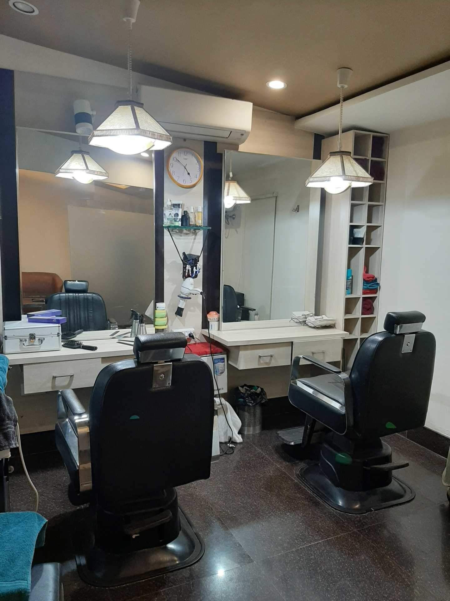 A salon with two black salon chairs, a white desk, a large mirror, and shelves with various items.
