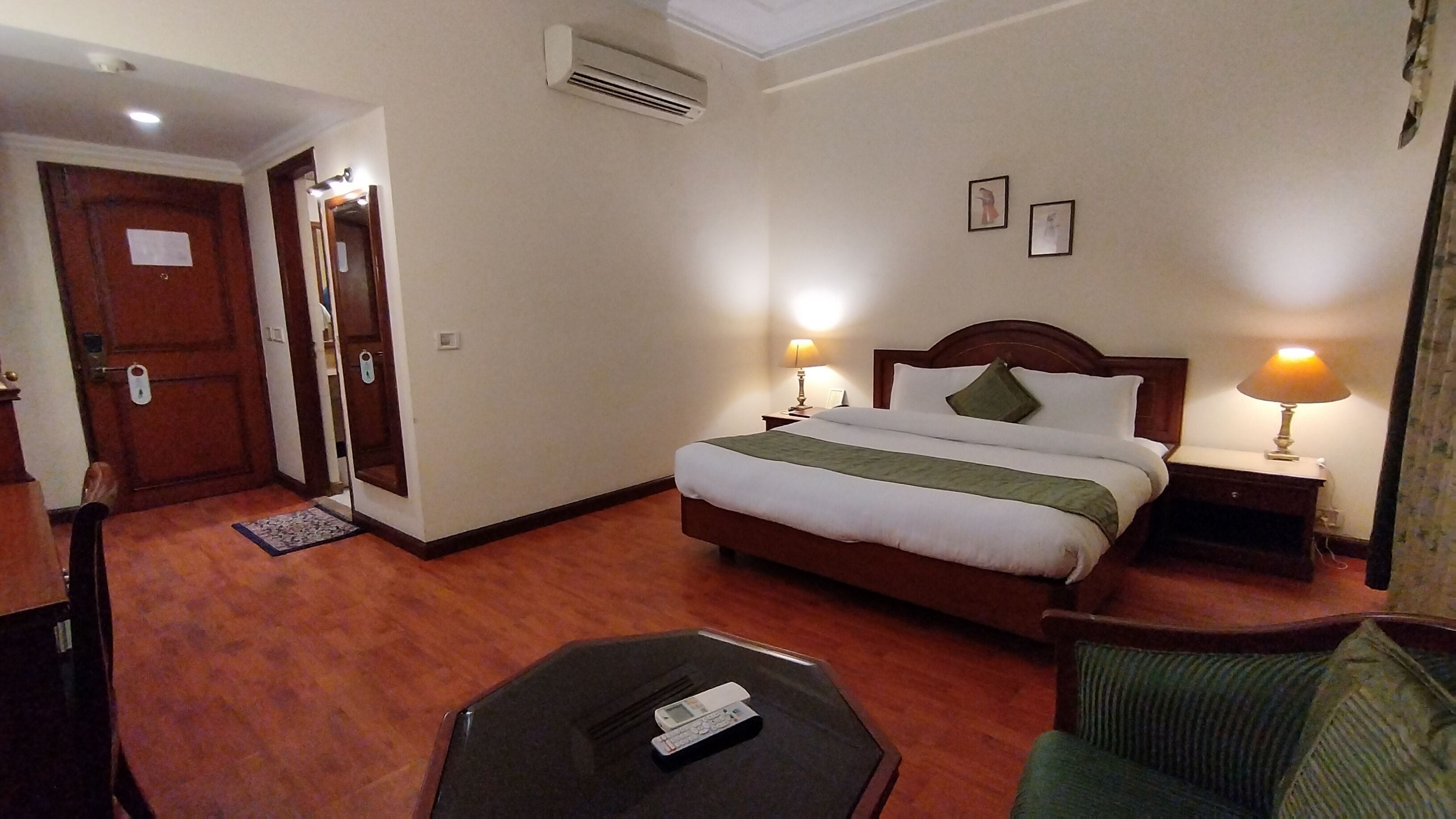 A hotel room with a bed, bedside lamps, a chair, a small table, and a door leading to another room.