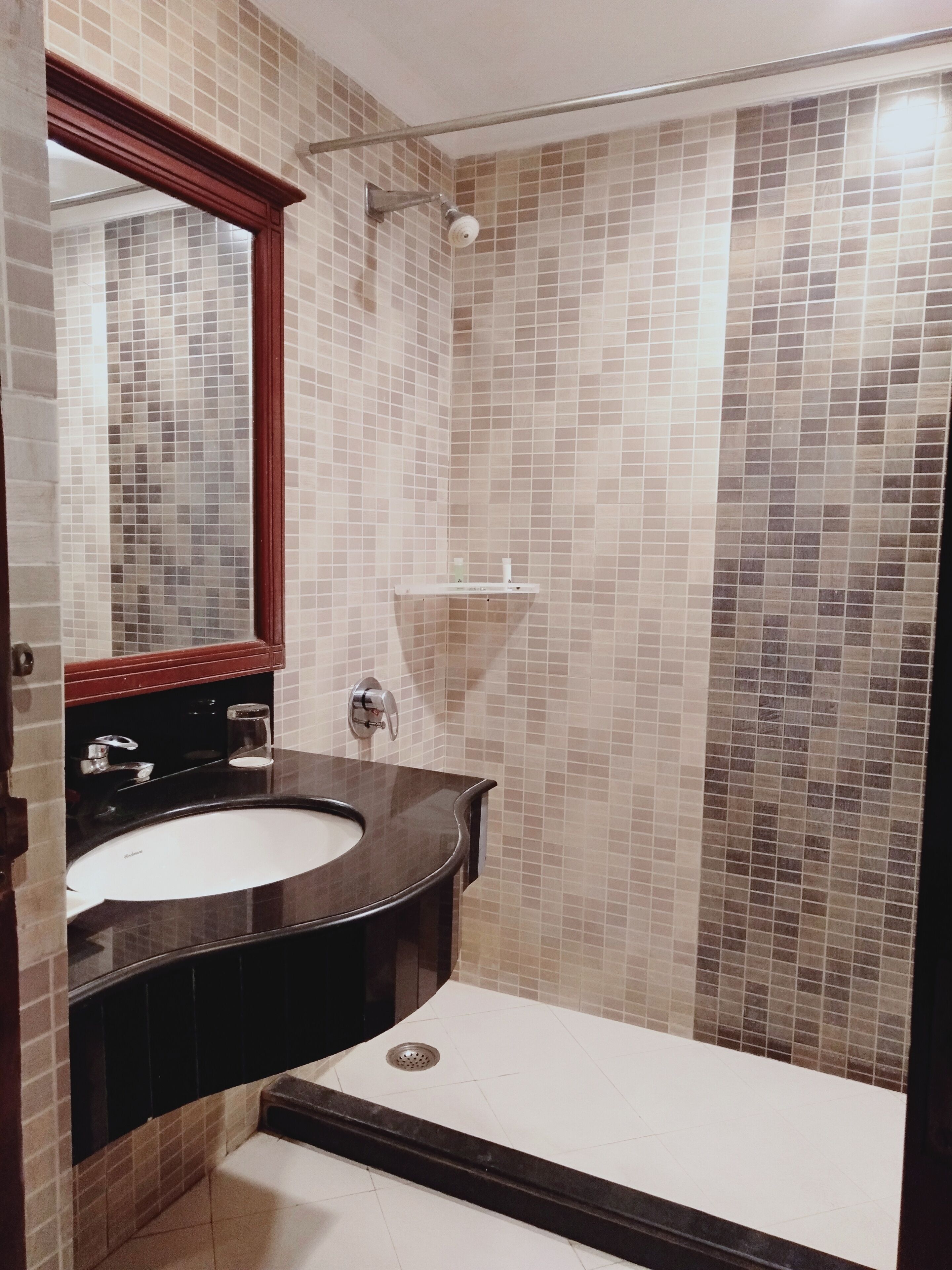 Een badkamer met een zwart wastafel, een spiegel, een douche met glazen deur en betegelde muren.