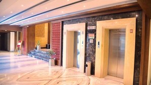 A hotel lobby with marble flooring, elevators, and a red patterned wall. - Hotel Sepal (Bathinda)