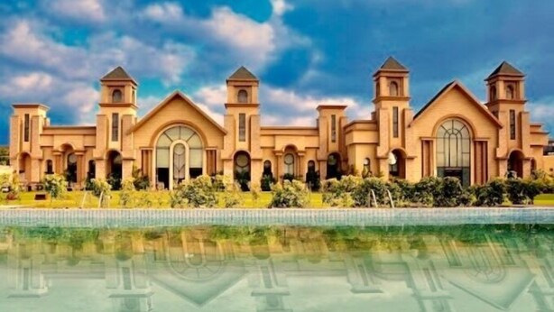 A large, multi-story building with arched windows and towers, surrounded by a pool and greenery. - Hotel Sepal (Bathinda)