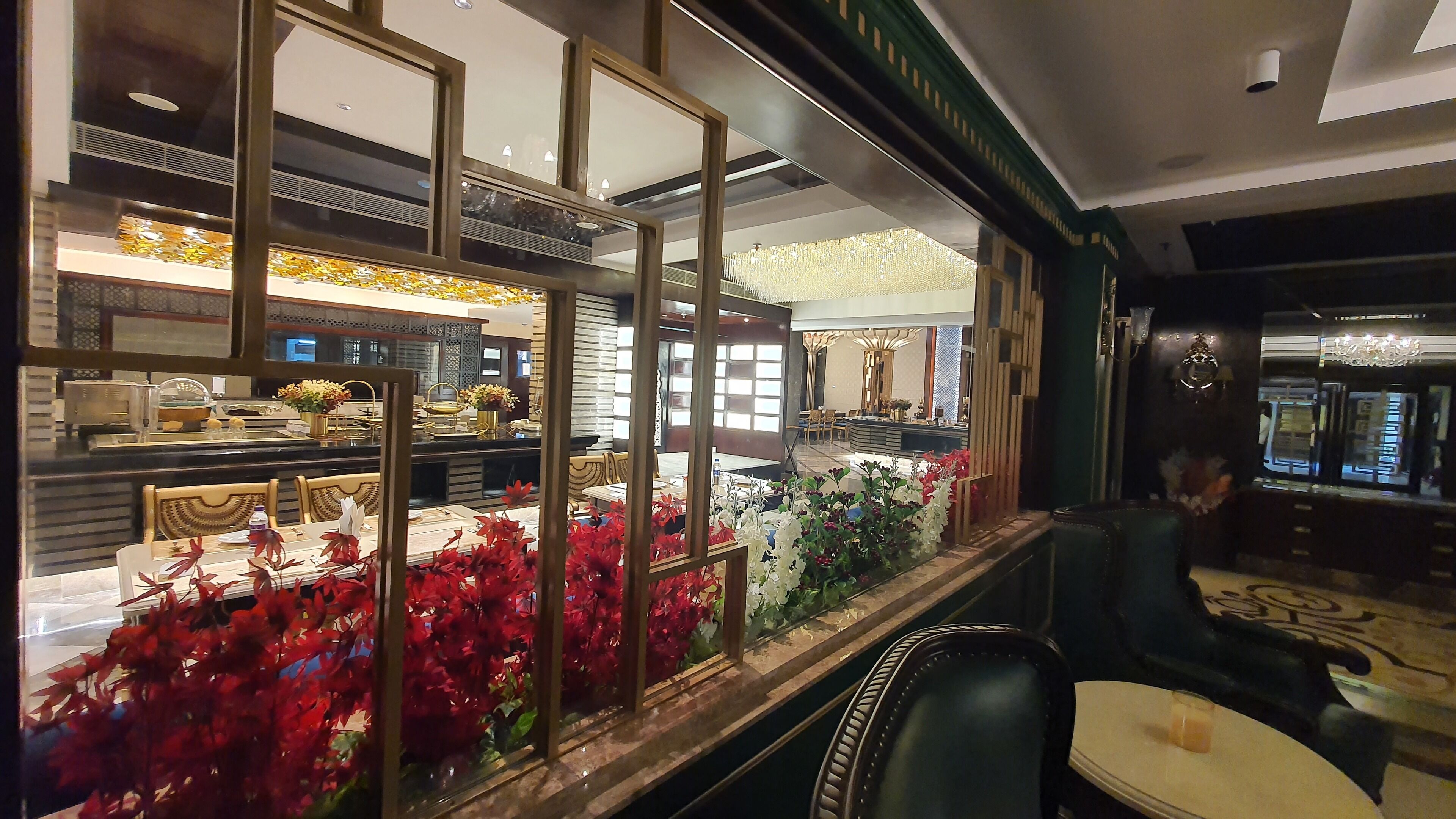 A restaurant interior with a dining area, a counter with a display case, and a decorative plant arrangement.