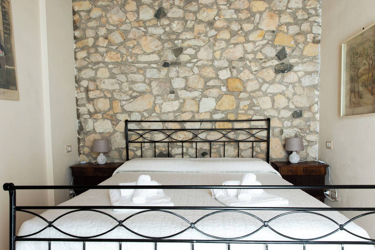 A bed with a stone wall backdrop, two bedside tables with lamps, and a metal bed frame.