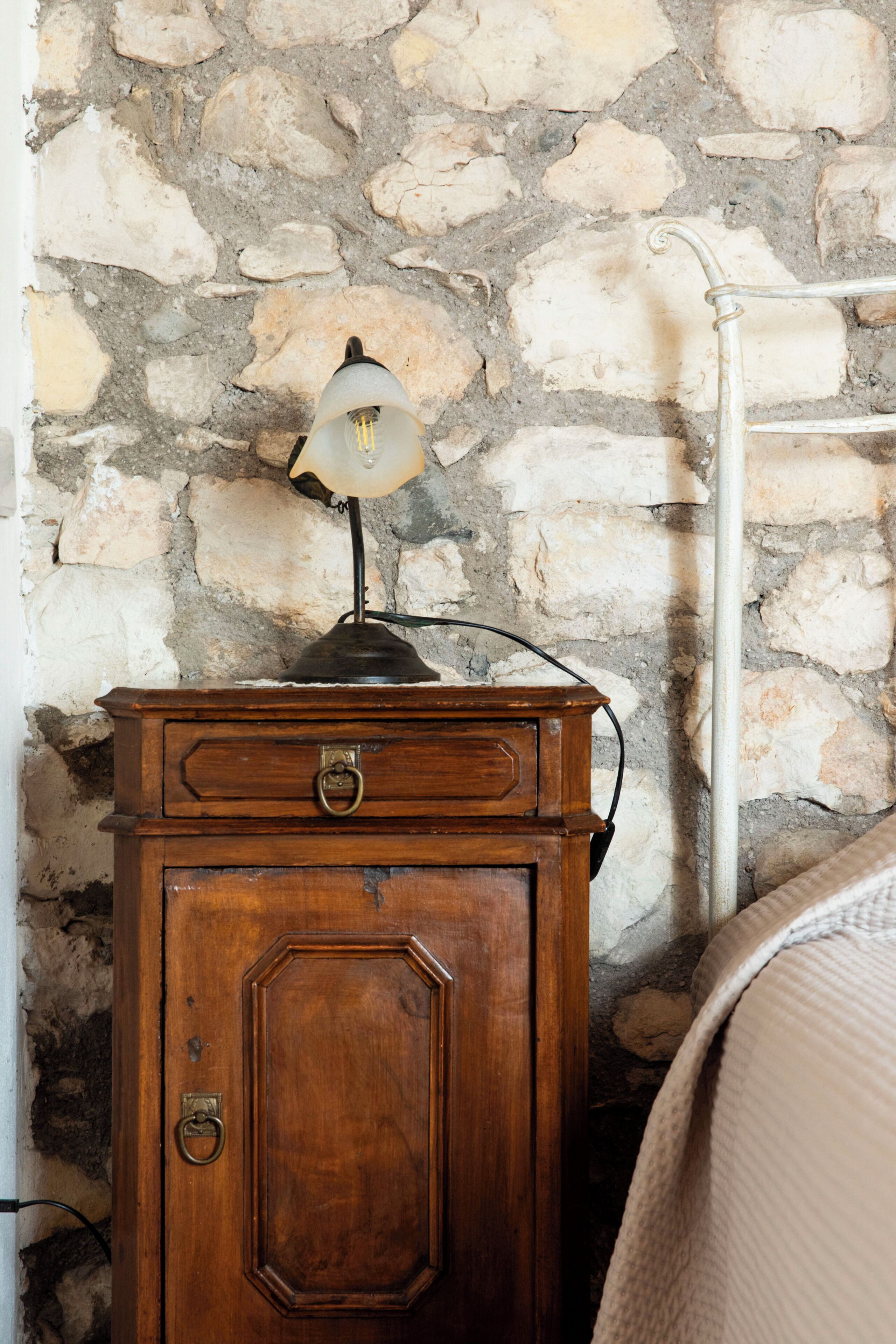 Une commode en bois, une lampe, un mur en pierre et un radiateur.