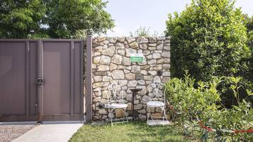 Un muro de piedra con un cartel de zona para fumadores, una reja de metal y dos sillas de metal blanco en un área con césped.