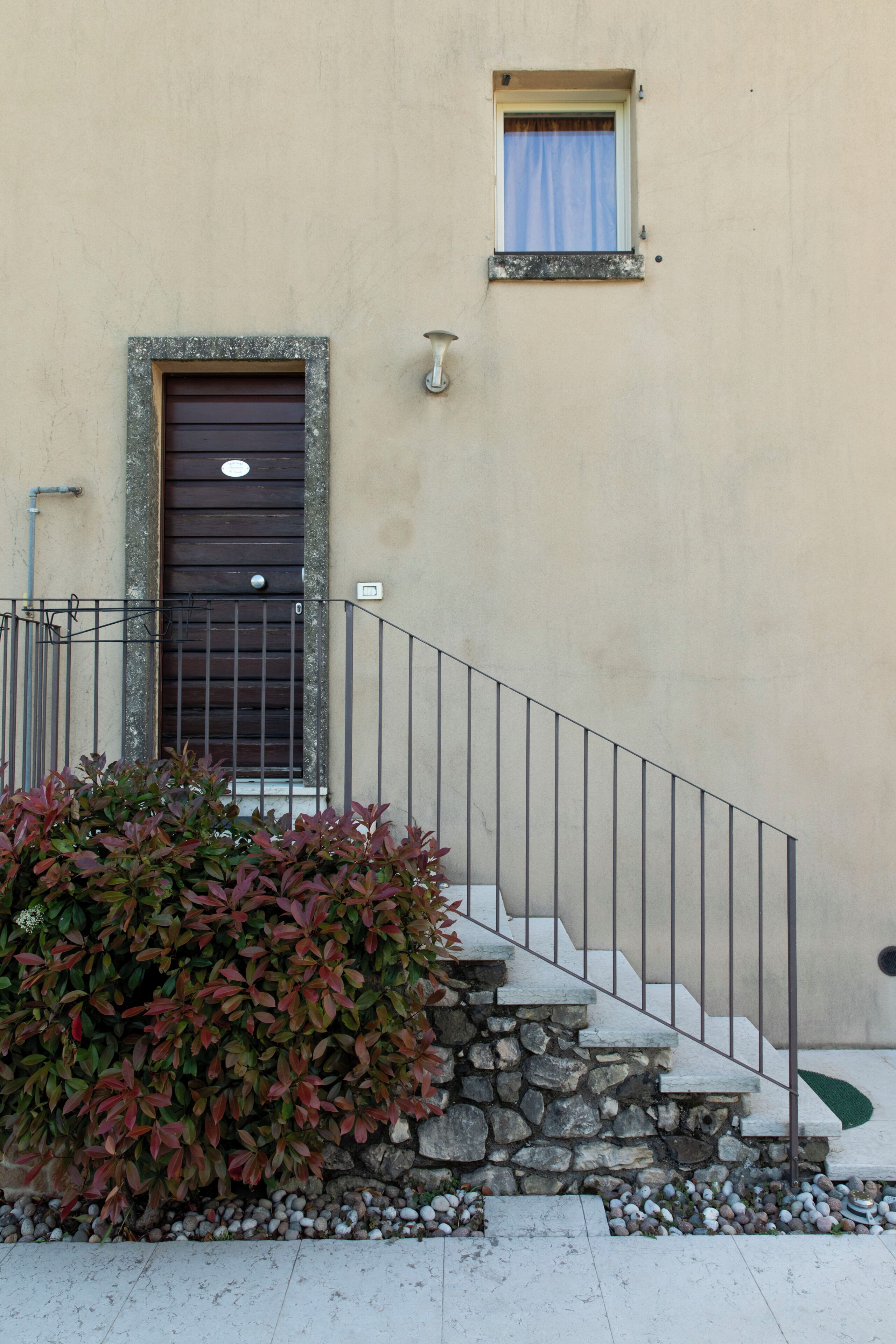 Un bâtiment doté d’un escalier en pierre, d’une rambarde en métal et d’une petite fenêtre avec un rideau.