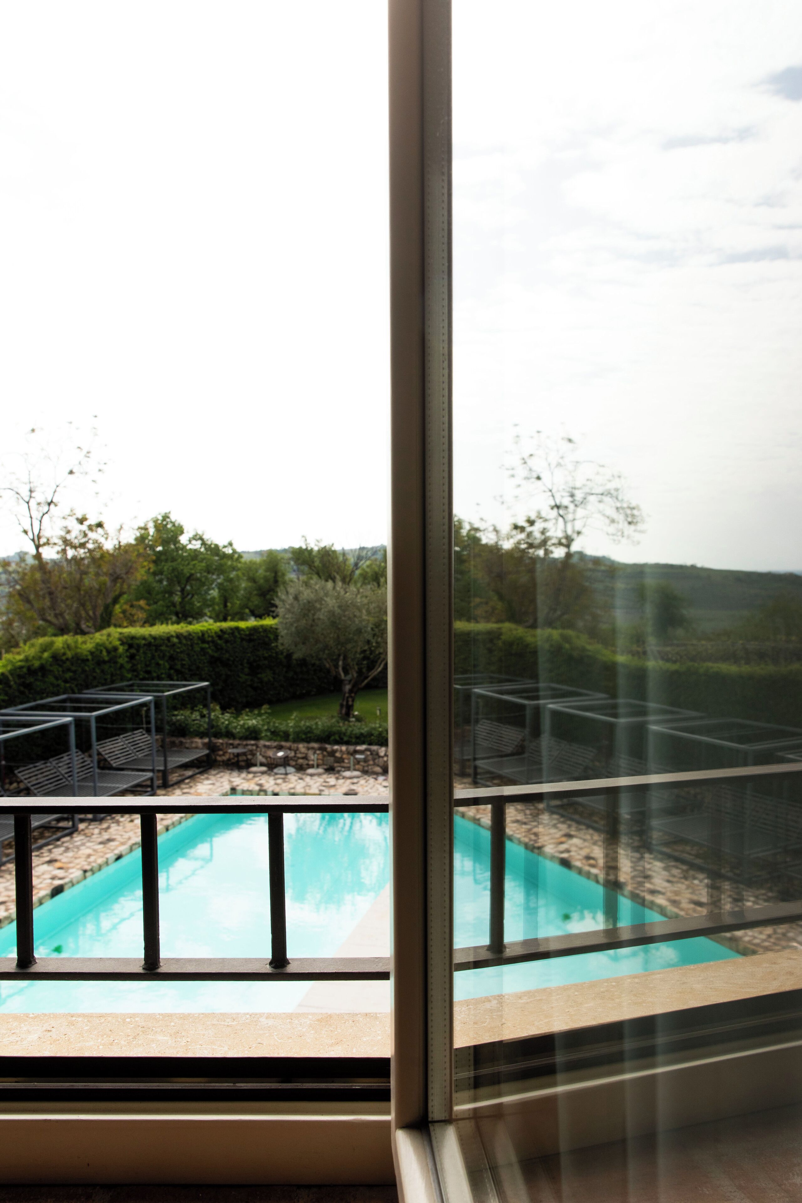 A pool with a metal frame and a view of a landscaped garden through a window.