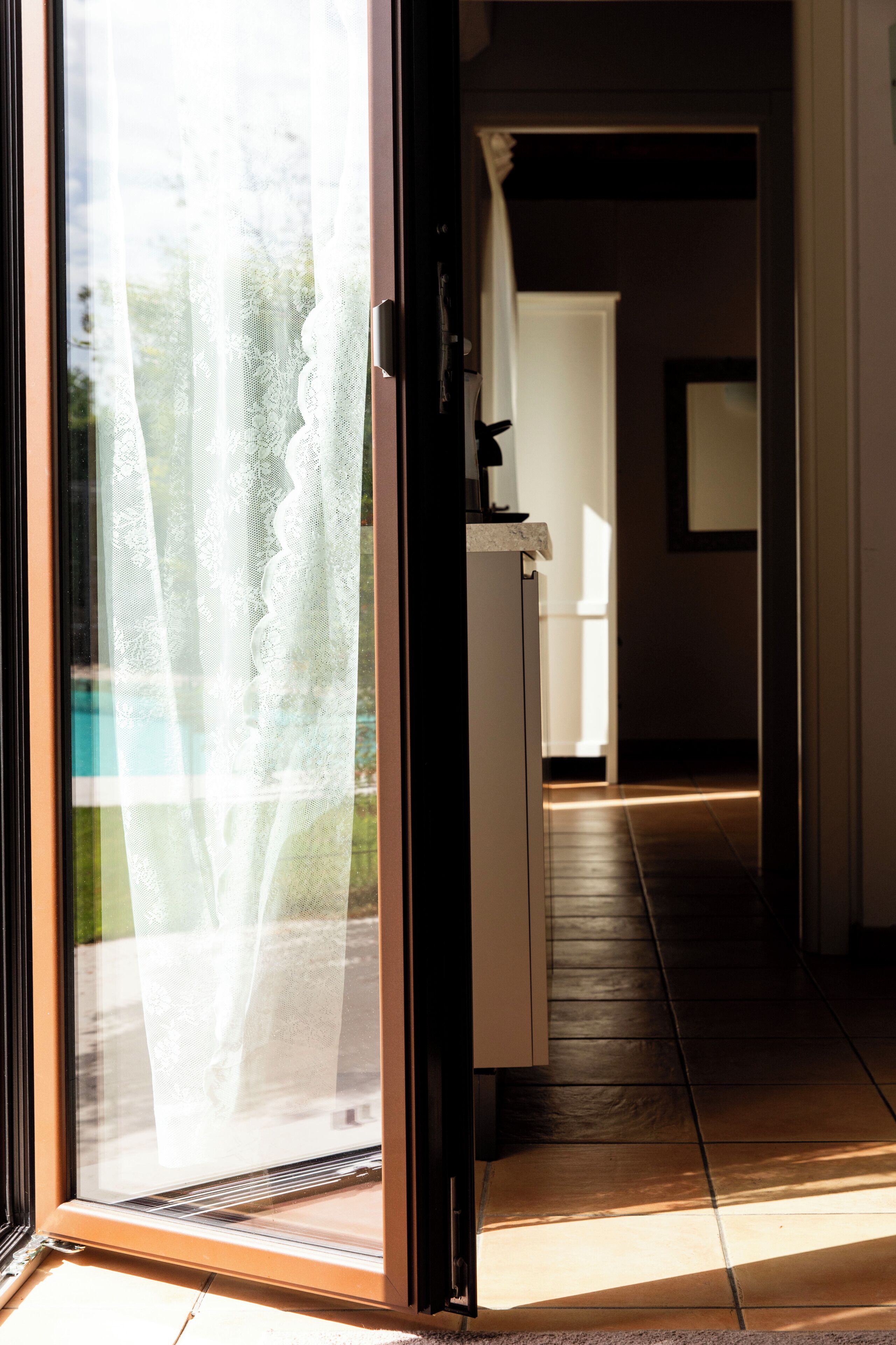 A hallway with a sliding glass door leading to a room, a white door at the end, and a small table with a lamp.