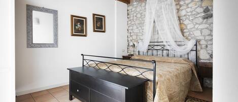 A bedroom with a bed, a nightstand, a dresser, and a stone wall.