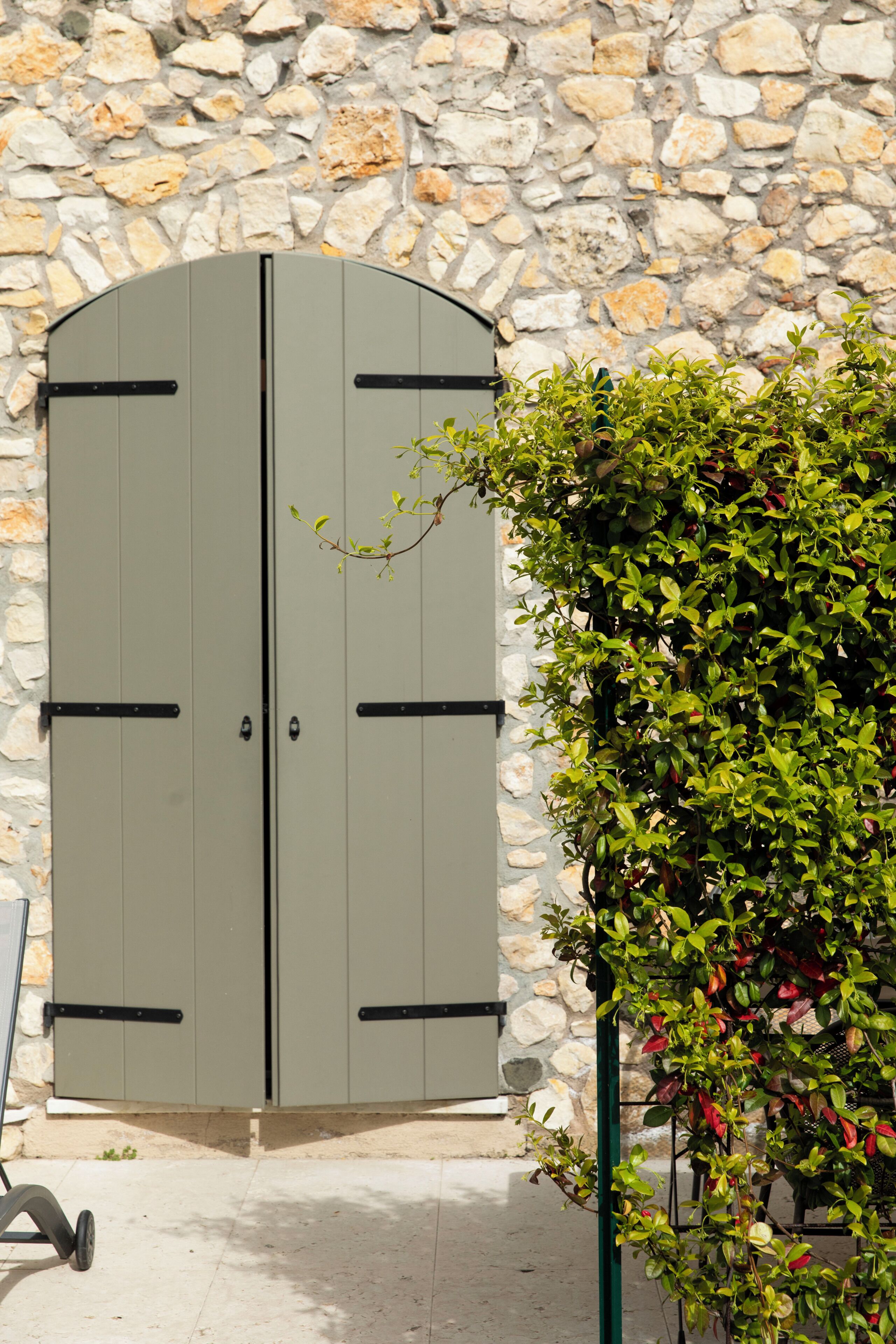 A double door with a stone wall background, a green plant to the right, and a chair in the foreground.