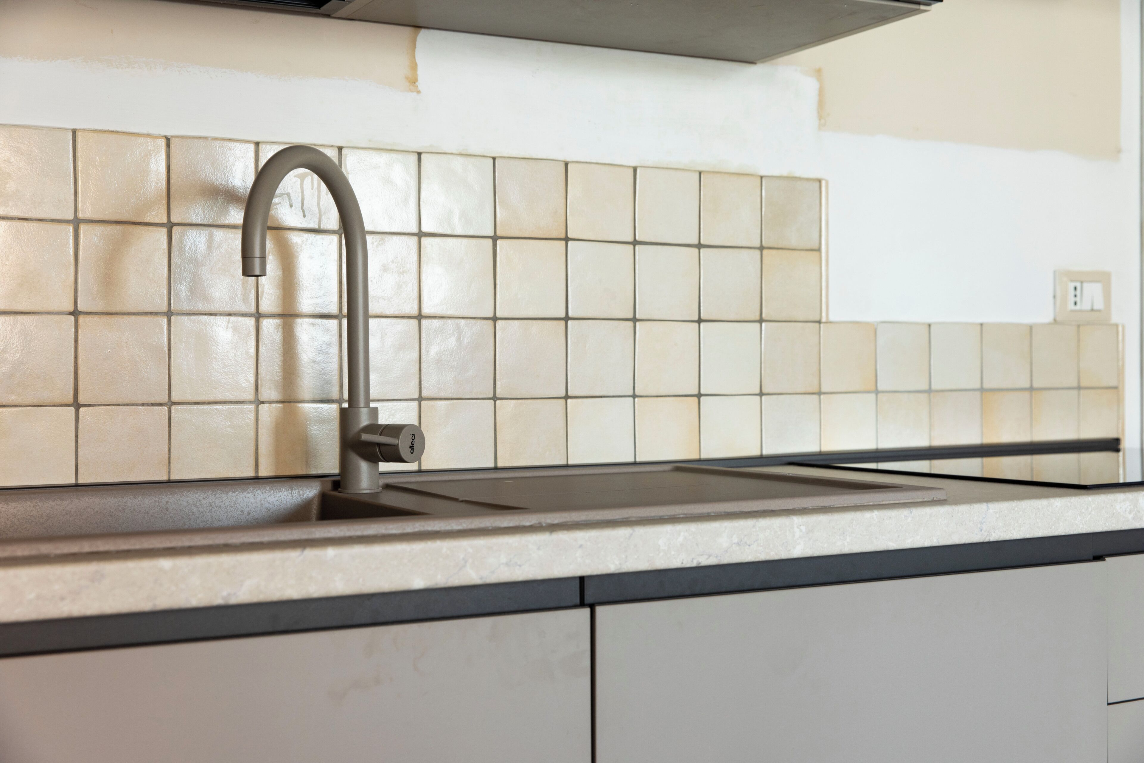 A kitchen with a modern faucet, a tiled backsplash, and a countertop.