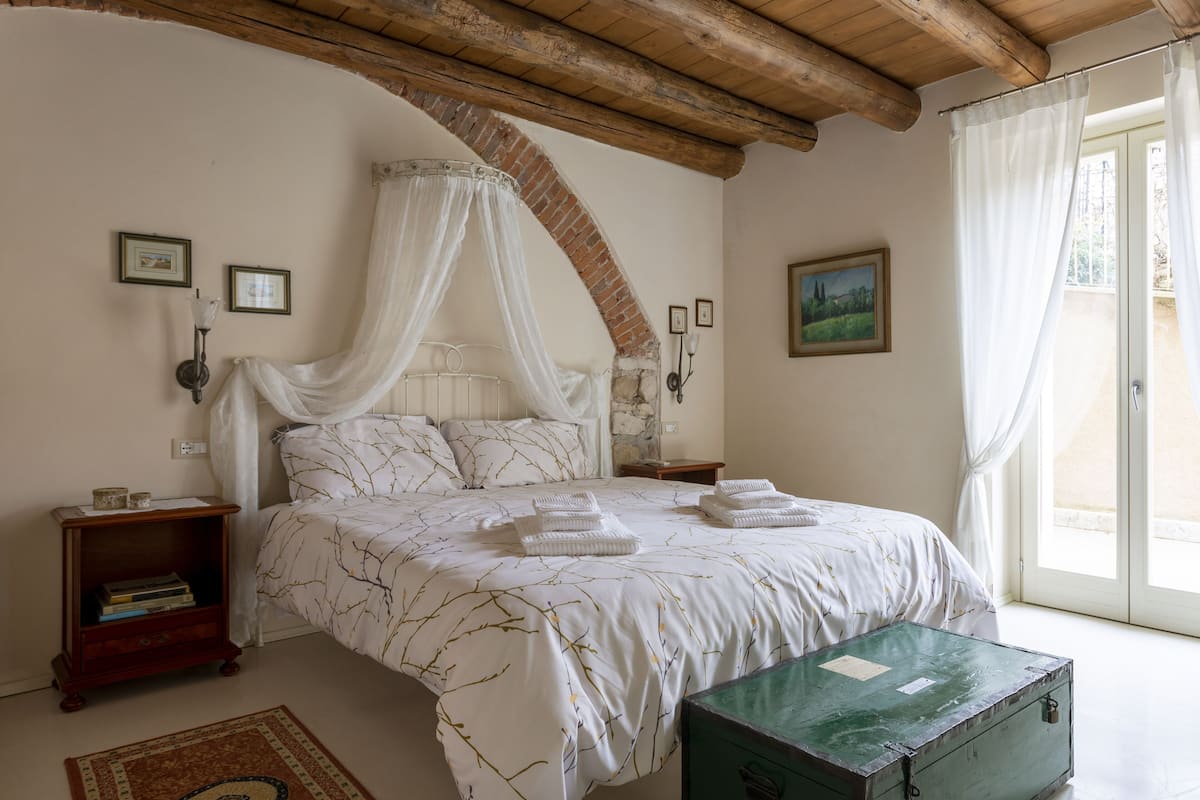 A bedroom with a four-poster bed, a green trunk, and a rustic ceiling.