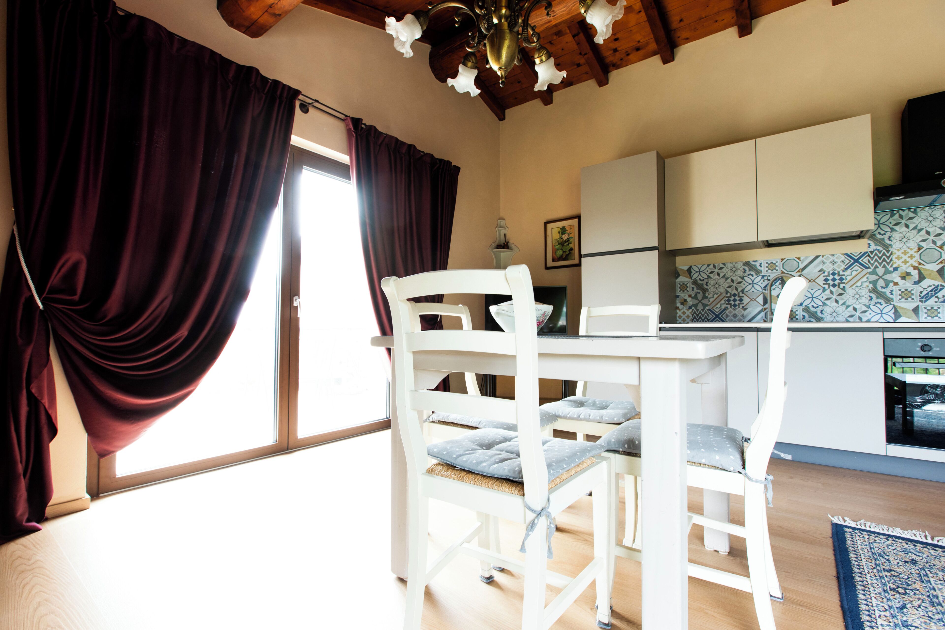 Ein Zimmer mit Esstisch, Stühlen, Küchenzeile und einem fenster mit Vorhängen.