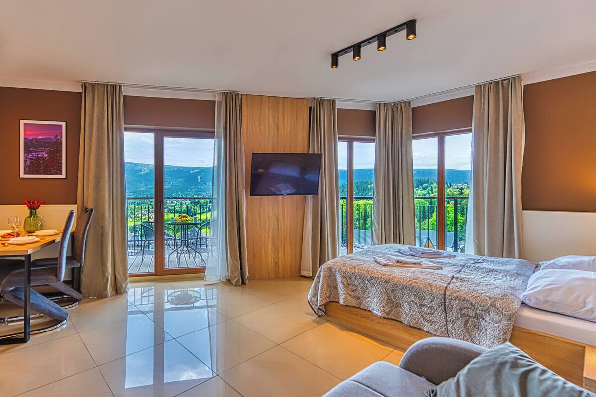 Una habitación de hotel con balcón, comedor, cama y televisor.