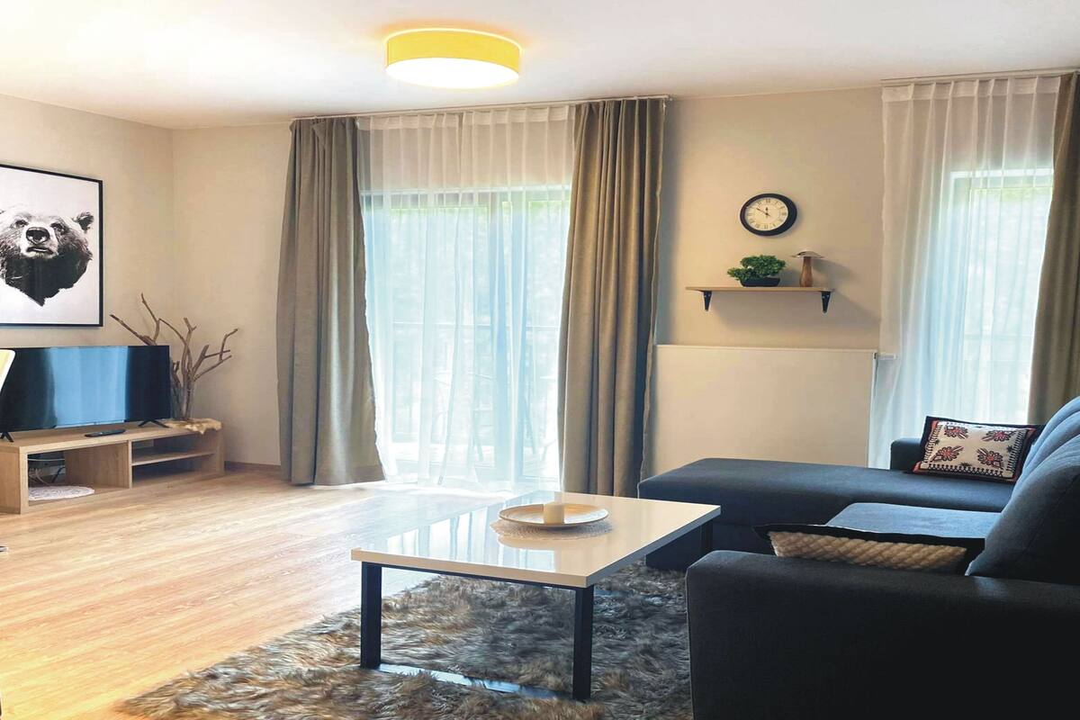 Una sala de estar moderna con un sofá, una mesa de centro, un televisor sobre un mueble bajo y un reloj en la pared.
