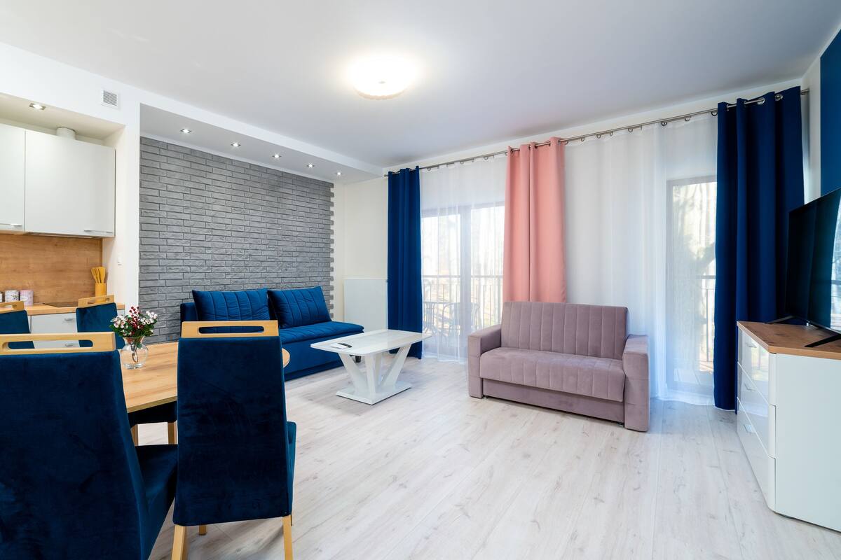 Una sala de estar moderna con un sofá, una mesa de centro y un televisor. Hay una zona de cocina con armarios y una encimera.