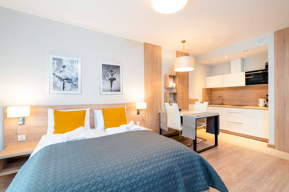 Una habitación de hotel moderna con una cama, mesitas de noche, un escritorio y una kitchenette.