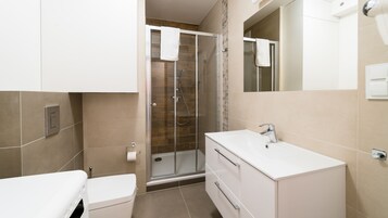 Un baño moderno con cabina de ducha de vidrio, un lavabo blanco y un inodoro.