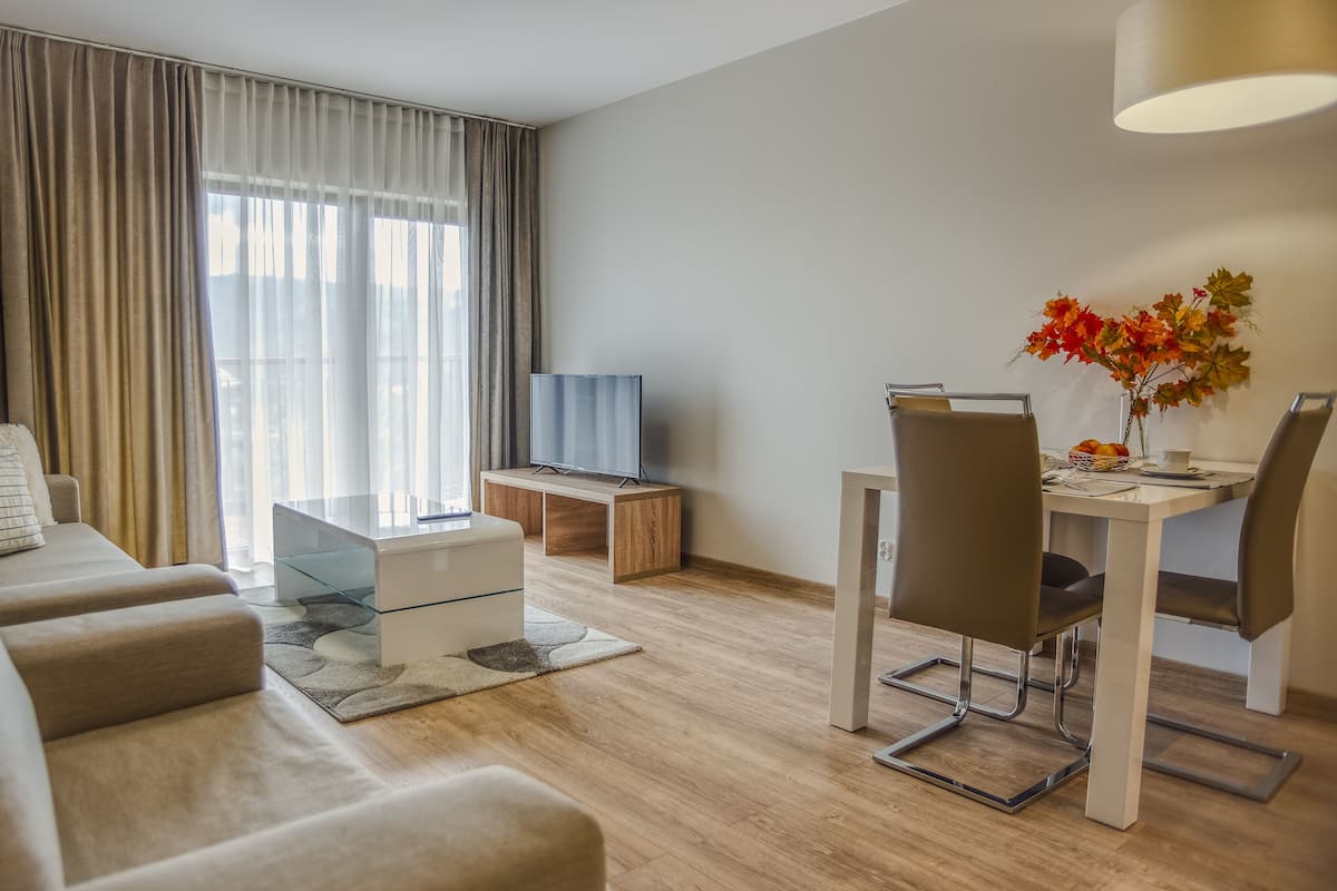 Una sala moderna con un sofá, una mesa de centro, un televisor sobre un soporte de madera, una mesa de comedor con sillas y un jarrón con hojas otoñales.