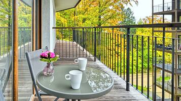 A balcony with a round table, two white cups, and a vase with pink flowers.