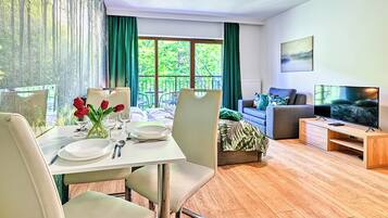 Een goed verlichte kamer met een eettafel gedekt voor twee personen, een bank, een televisie en een bed.