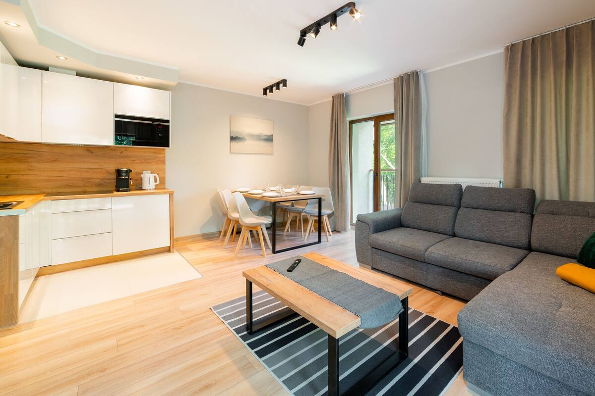 Una sala de estar moderna con un sofá gris, una mesa de centro de madera y un comedor con mesa y sillas.