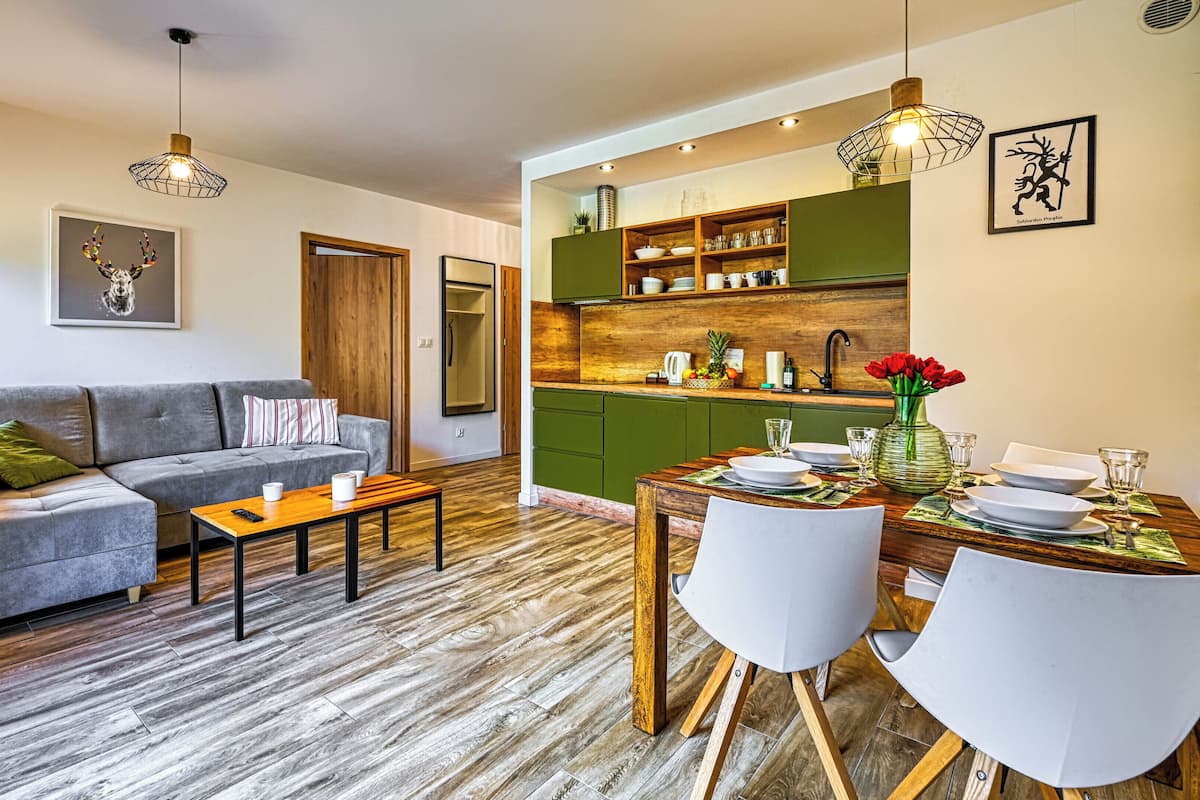 Una sala de estar moderna con un sofá gris, una mesa de centro de madera y una zona de comedor con una mesa de madera preparada para dos personas.