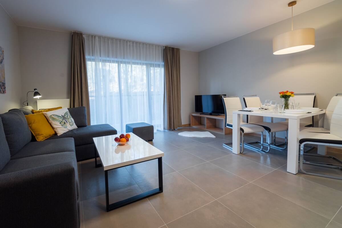 Una sala de estar moderna con sofá, mesa de centro y zona de comedor con sillas y televisor.