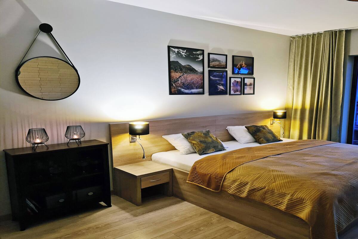 Habitación de hotel con una cama grande, dos mesitas de noche, un cabecero y vistas a un balcón.