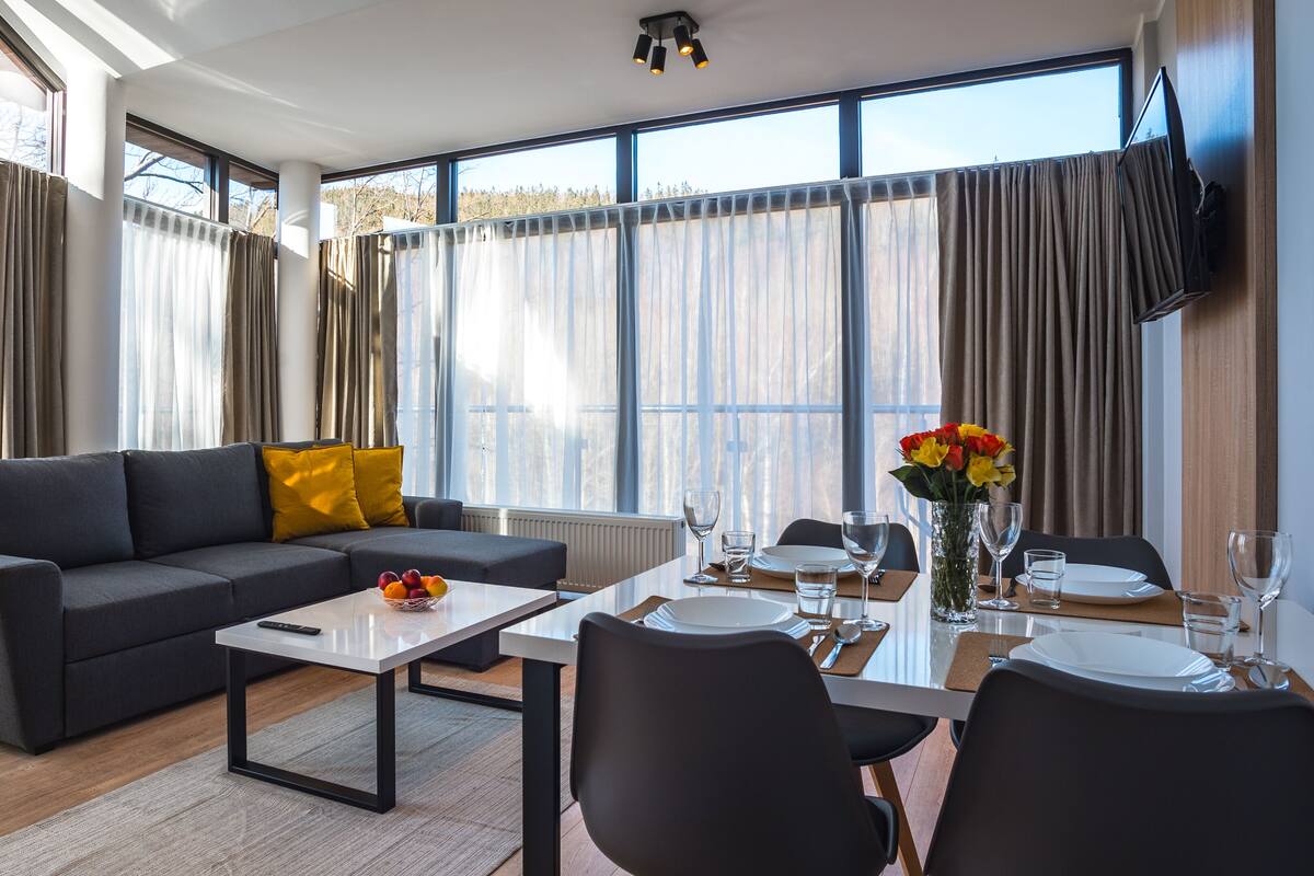 Una sala de estar moderna con un sofá gris, una mesita de centro y un comedor con una mesa preparada para dos.