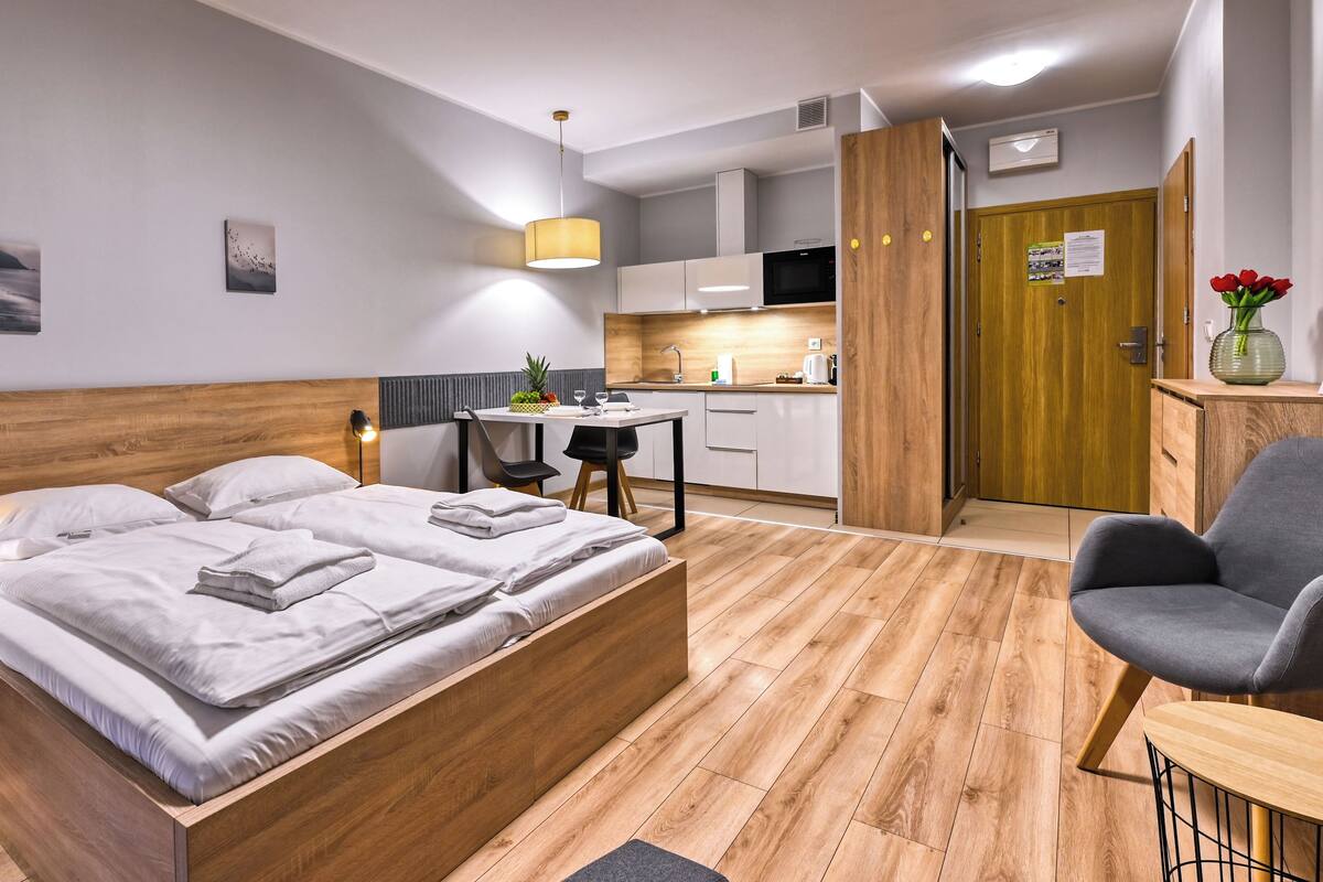 Una habitación de hotel moderna con una cama de madera, un pequeño escritorio, una silla, una kitchenette y un baño.
