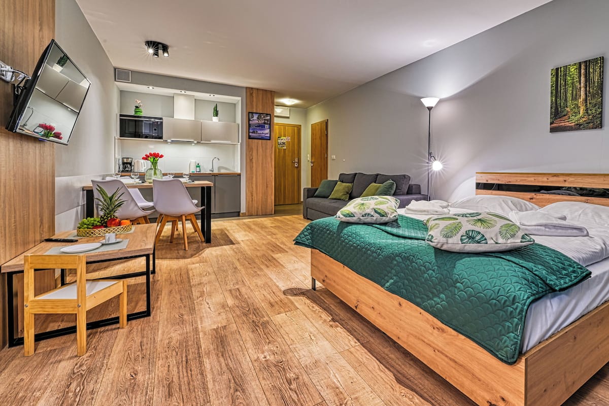 Un dormitorio moderno con una cama de madera, un escritorio con silla, un sofá y una mesa de comedor con sillas.