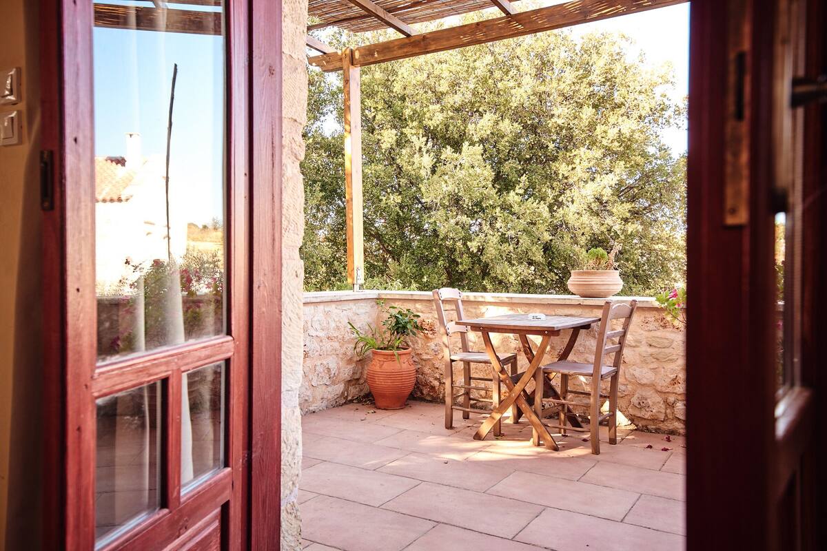 Un patio al aire libre con una mesa y sillas de madera, una planta en maceta y un muro de piedra.