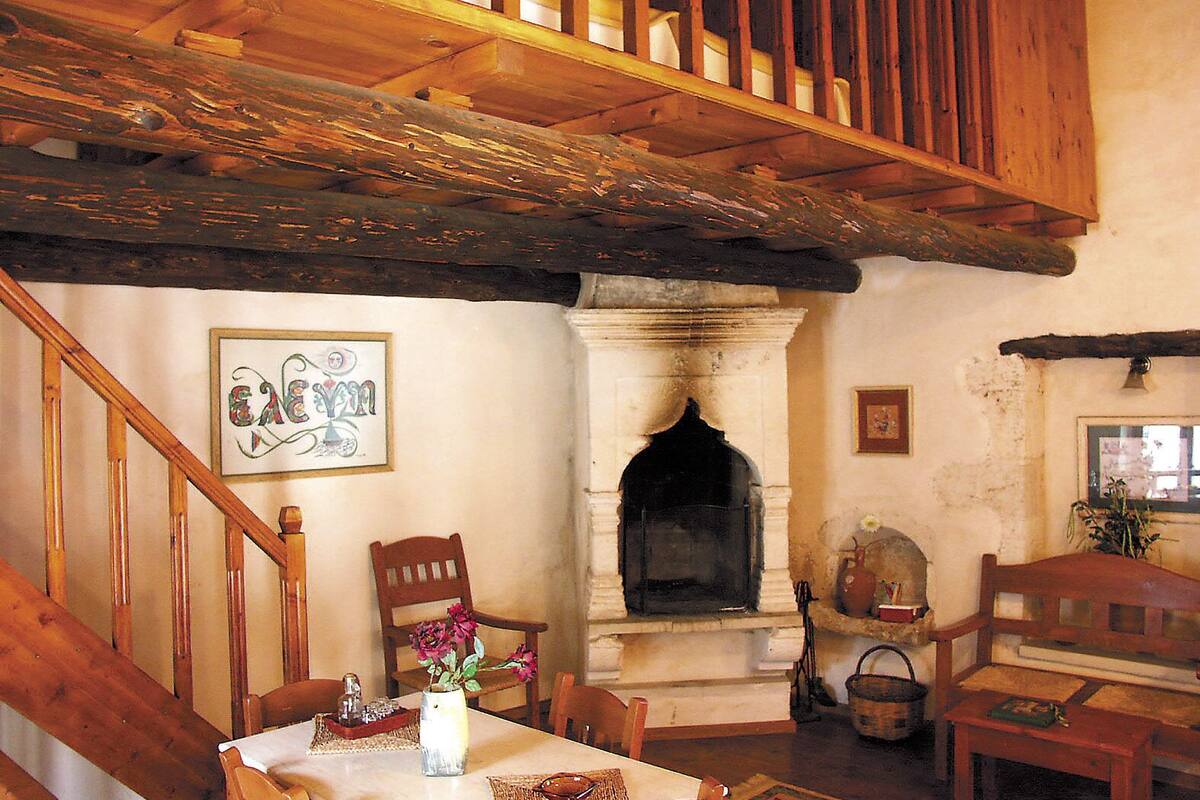 Un interior rústico con una escalera de madera, una chimenea y un comedor con mobiliario de madera.