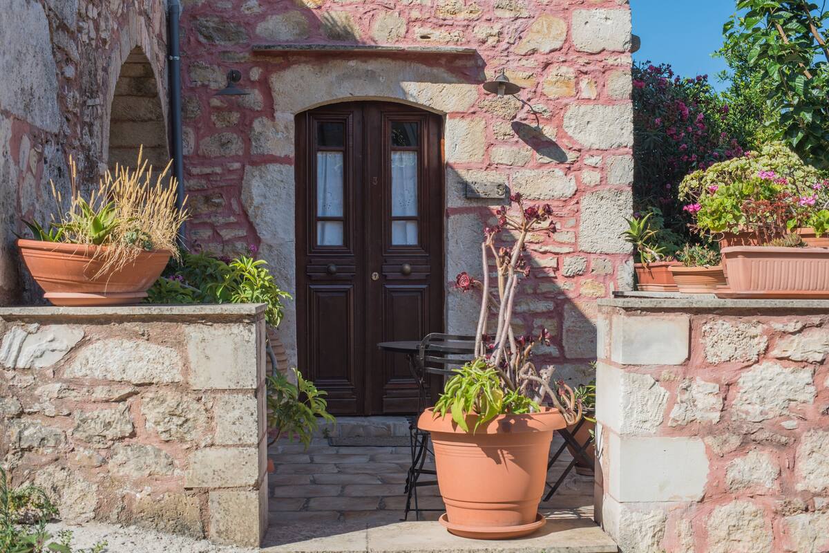 Un edificio de piedra con puerta de madera, plantas en macetas y una pequeña mesa.