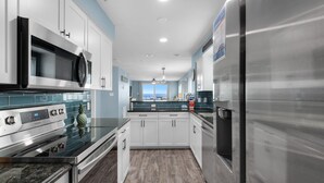 Una cocina moderna con electrodomésticos de acero inoxidable, armarios blancos y vistas al exterior.