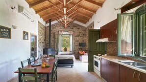 A rustic kitchen with stone walls, wooden beams, and a dining area with a table and chairs. - Authentic Cottage in a heaven of natural Beauty (Sempronas / Chania)