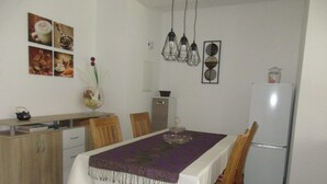 A dining area with a table set for four, wooden chairs, a white tablecloth, and a purple runner. There are wall-mounted light fixtures above the table and a refrigerator to the right. - Vacation apartment "Zum alten Pferdestall" - Somewhere in the middle of nowhere (Zichow)