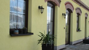 A building with yellow walls, multiple windows with dark frames, and outdoor lighting fixtures. - Vacation apartment "Zum alten Pferdestall" - Somewhere in the middle of nowhere (Zichow)