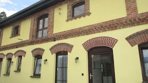A building with yellow walls, brick accents, and multiple windows with shutters. - Vacation apartment "Zum alten Pferdestall" - Somewhere in the middle of nowhere (Zichow)