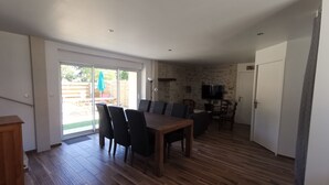 Een ruime woonkamer met een houten eettafel en stoelen, een stenen muur, een flatscreen televisie en een schuifdeur naar een terras.