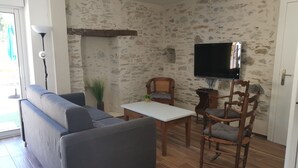 Een woonkamer met een grijze bank, een houten tafel en een aan de muur bevestigde televisie.