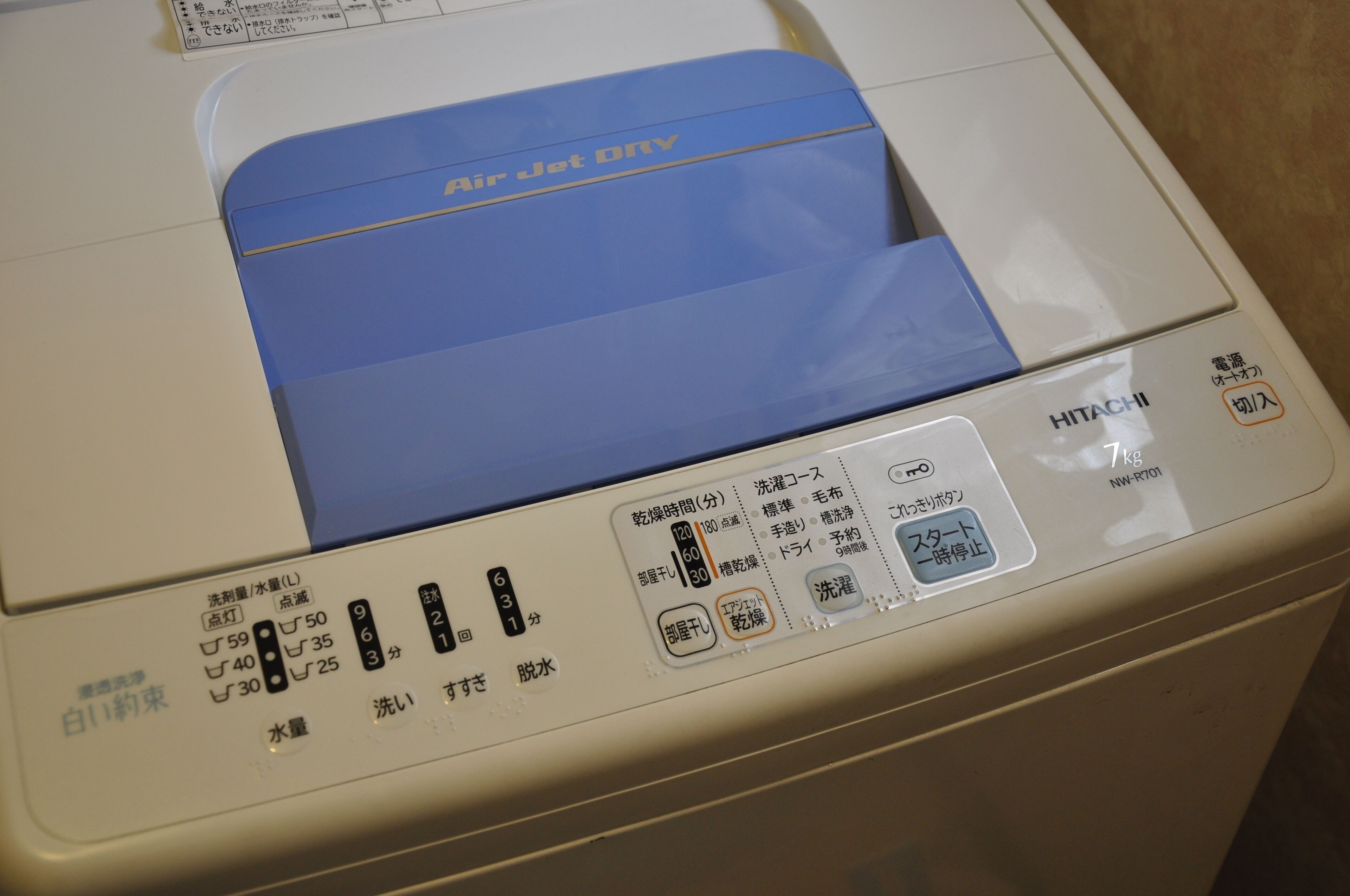 Une machine à laver à chargement frontal, avec un intérieur bleu, un panneau de commande avec des instructions en japonais et une capacité de 7 kg.