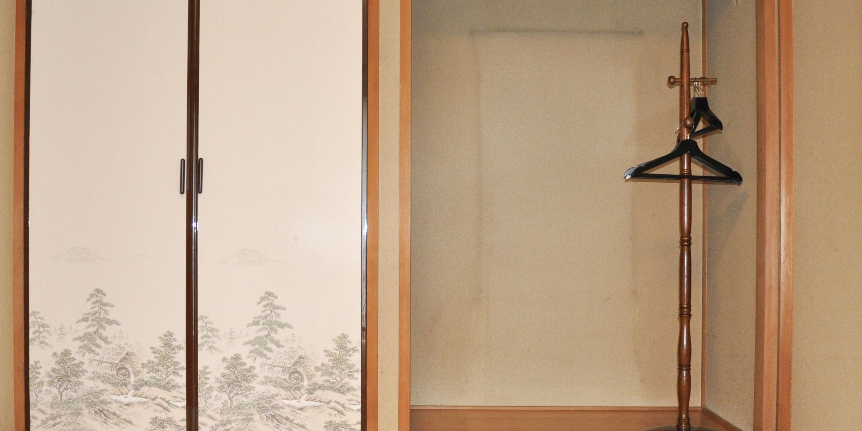 A room with a sliding door featuring a traditional landscape painting, a wooden floor, and a black hanger on a wooden stand.